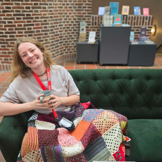 Ung kvinde i sofa på bibliotek med kaffe og bøger 