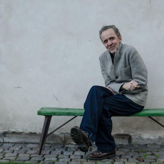 Kim Fupz Aakeson sidder udendørs på en grøn bænk foran en lys mur.