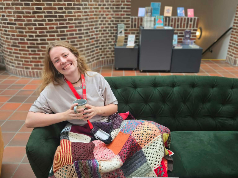 Ung kvinde i sofa på bibliotek med kaffe og bøger 