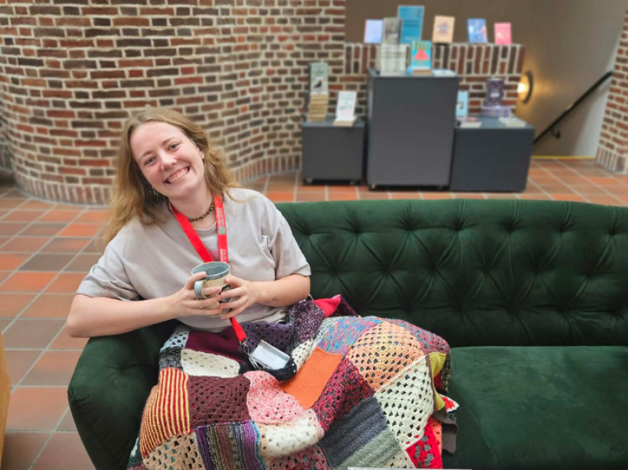 Ung kvinde i sofa på bibliotek med kaffe og bøger 